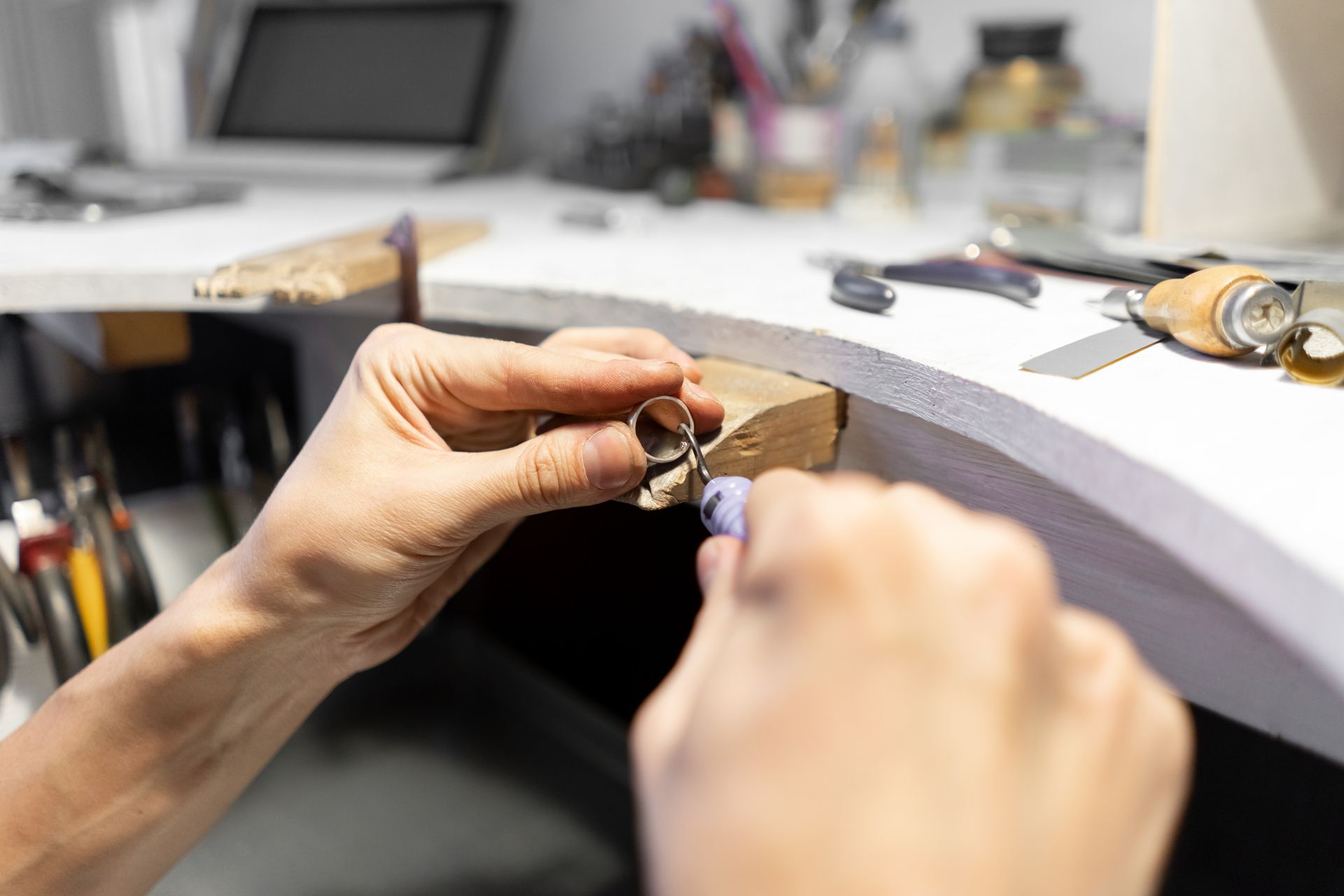 Des mains travaillant sur un petit bijou posé sur un établi dans un atelier