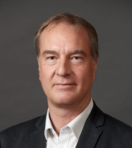 Ein Mann in Anzug und weissem Hemd schaut in die Kamera.