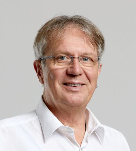 Ein Mann mit Brille und weissem Hemd lächelt in die Kamera.