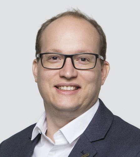 Ein Mann mit Brille und Anzug lächelt in die Kamera.