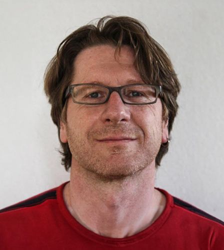 Ein Mann mit Brille und rotem Hemd lächelt in die Kamera.