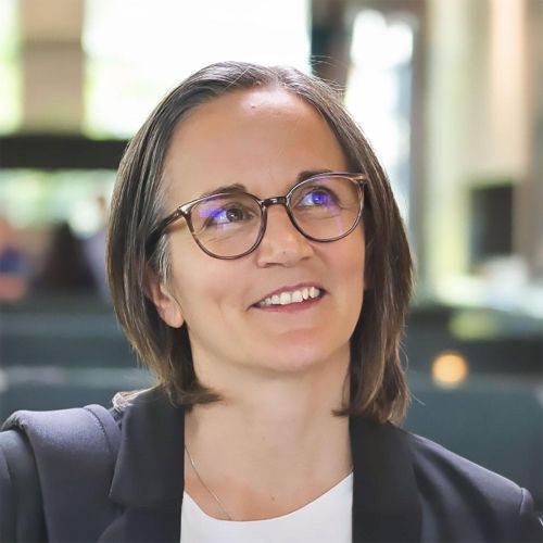 Eine Frau mit Brille und Jacke lächelt.