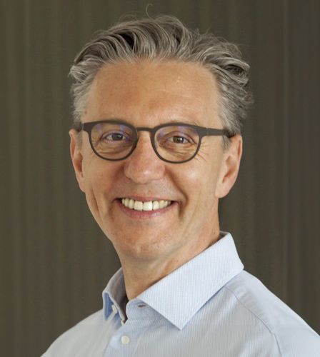 Ein Mann mit Brille und blauem Hemd lächelt in die Kamera.