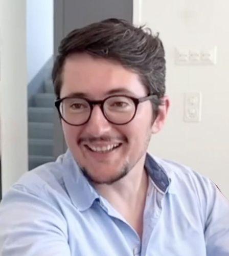 Ein Mann mit Brille und blauem Hemd lächelt.