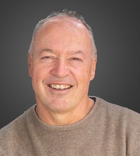 Ein Mann in einem braunen Pullover lächelt in die Kamera.