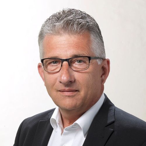 Ein Mann mit Brille und Anzug schaut in die Kamera.
