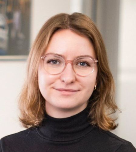 Eine Frau mit Brille und schwarzem Rollkragenpullover lächelt in die Kamera.