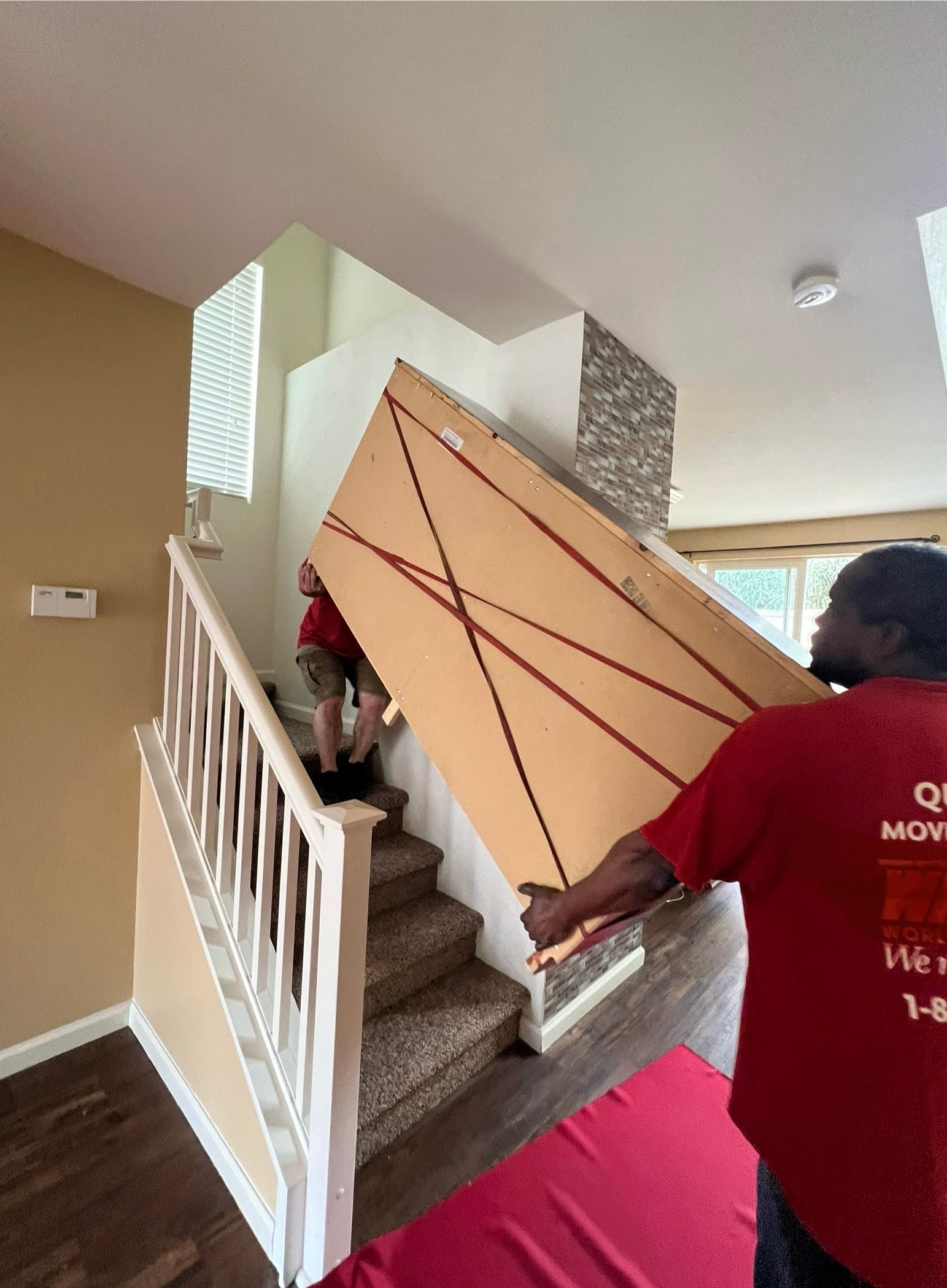 A man in a red shirt is carrying a large piece of wood