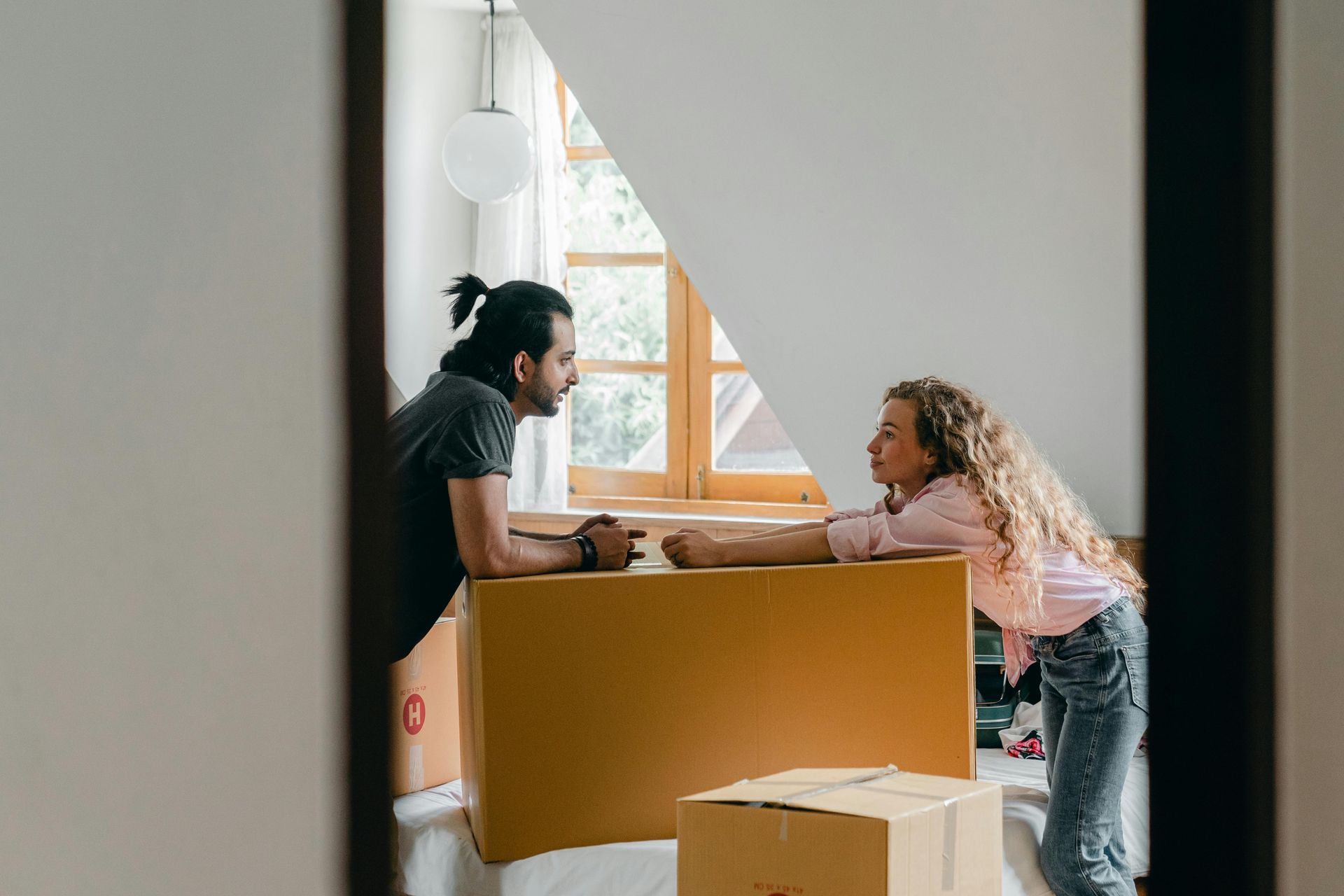 A man and a woman are pushing a cardboard box in a room.