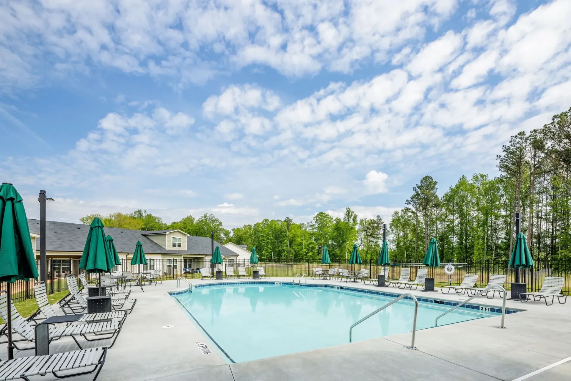 Outdoor swimming pool with lounge chairs and umbrellas under a blue sky with clouds.