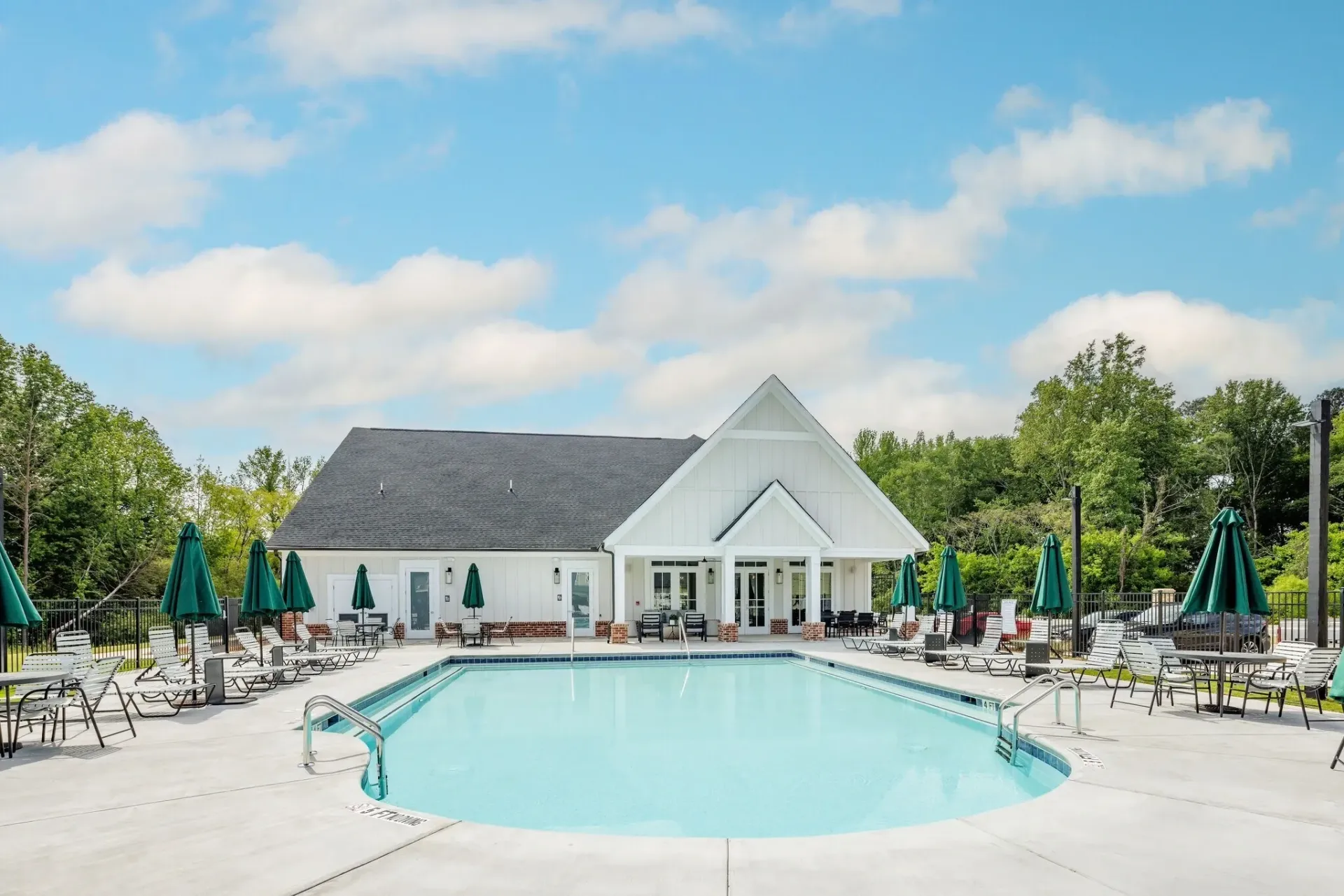 Outdoor swimming pool with lounge chairs and umbrellas next to a white building with a gabled roof.