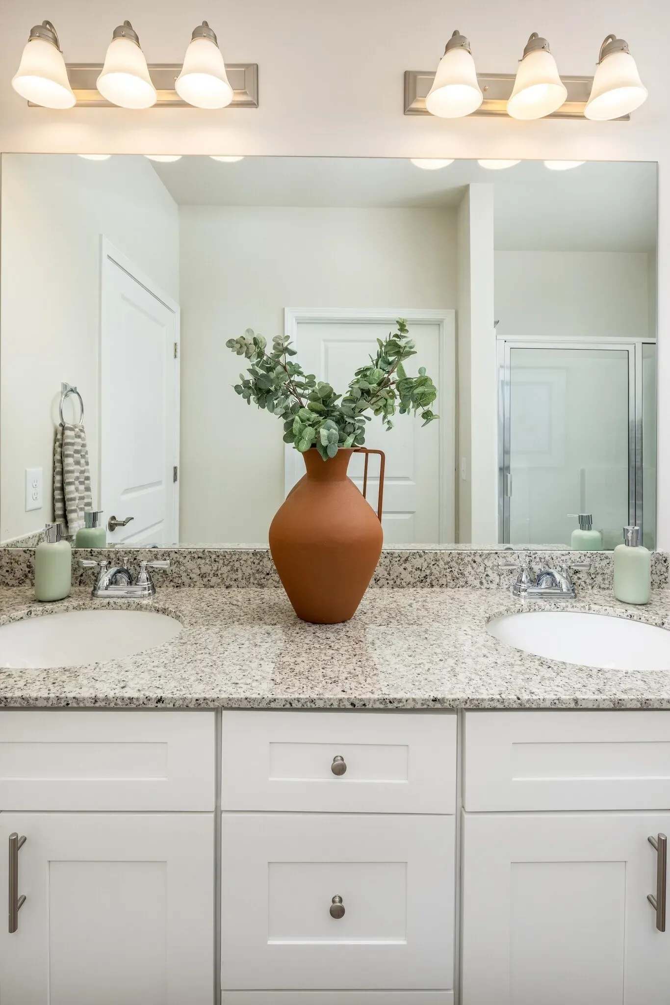 Double vanity with granite countertops, modern lighting, and decorative vase.