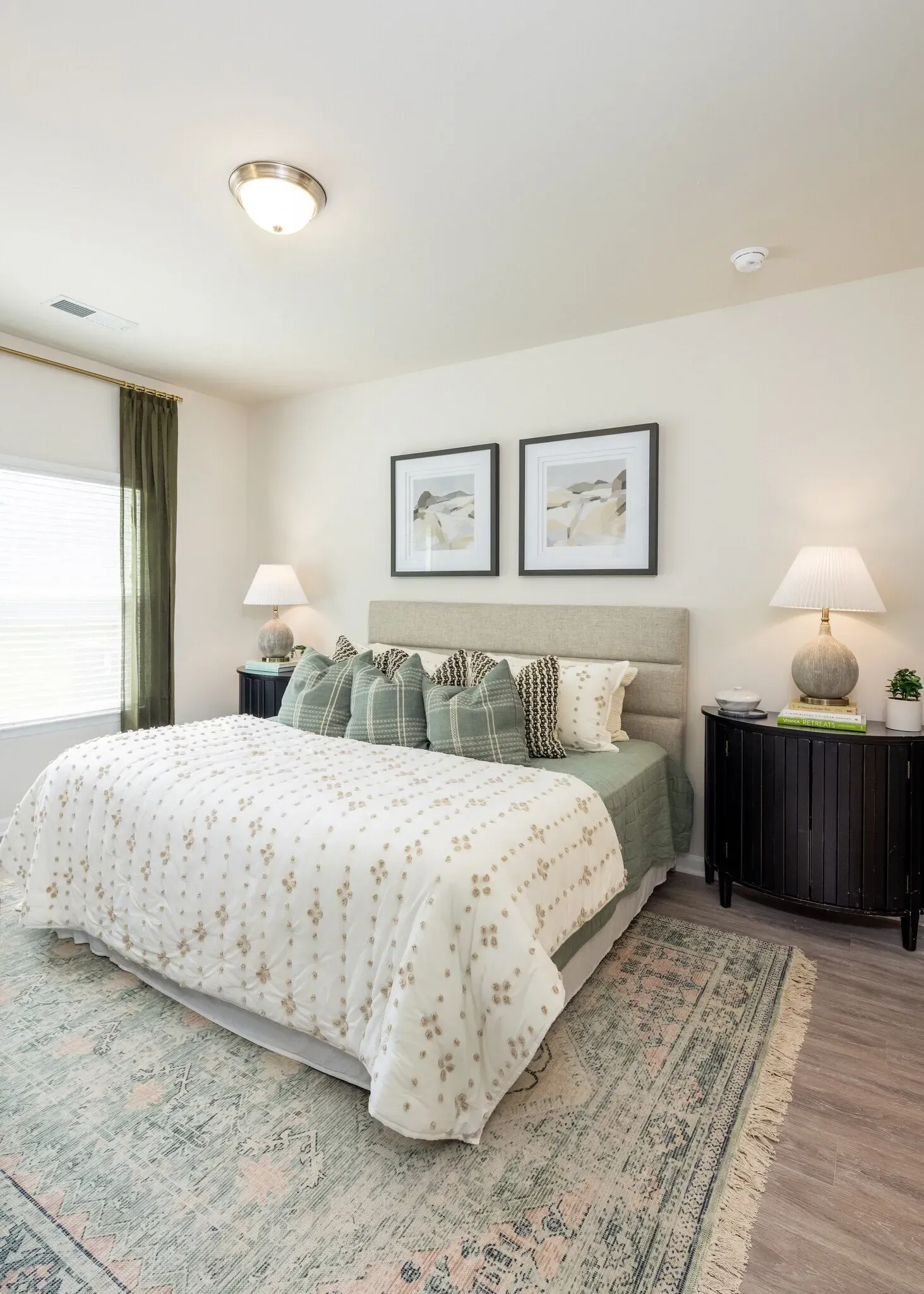 A king-sized bed with a textured white comforter and green pillows in a well-lit bedroom.