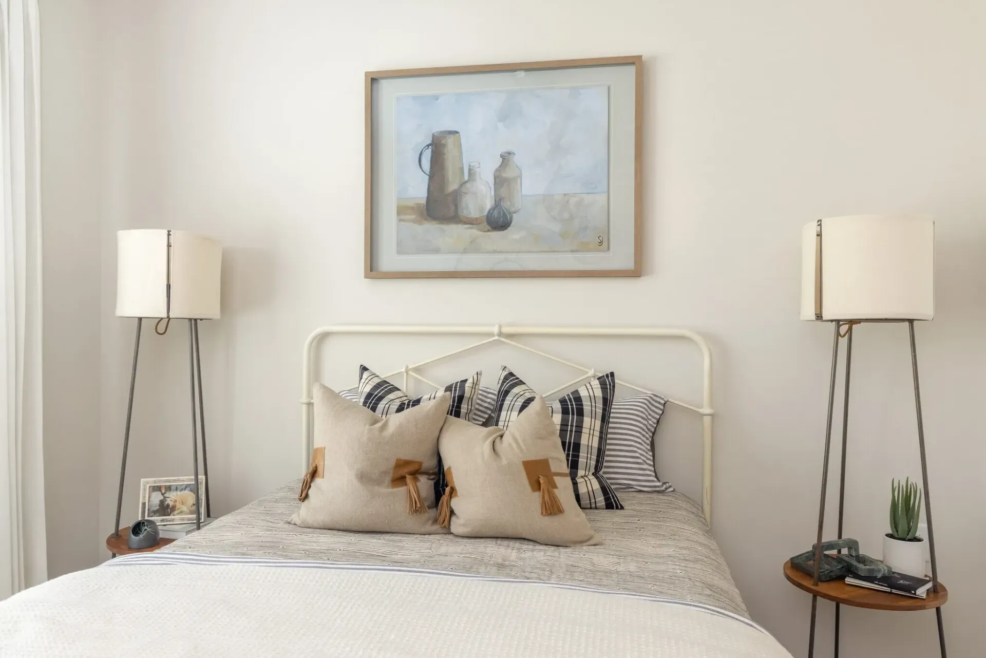 Bedroom with a queen-sized bed, decorated with neutral-toned pillows and a framed still-life painting above.