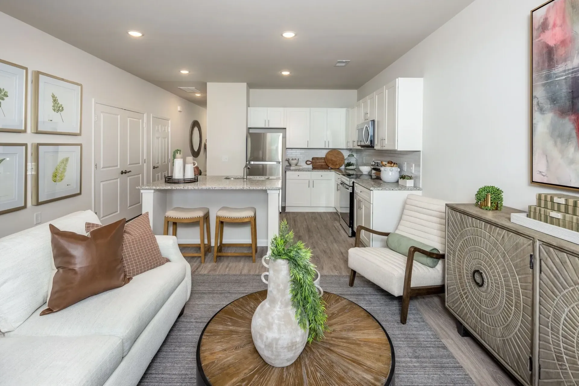 Interior view of a modern apartment living room and kitchen area with white furniture, granite countertops, and stainless steel appliances.