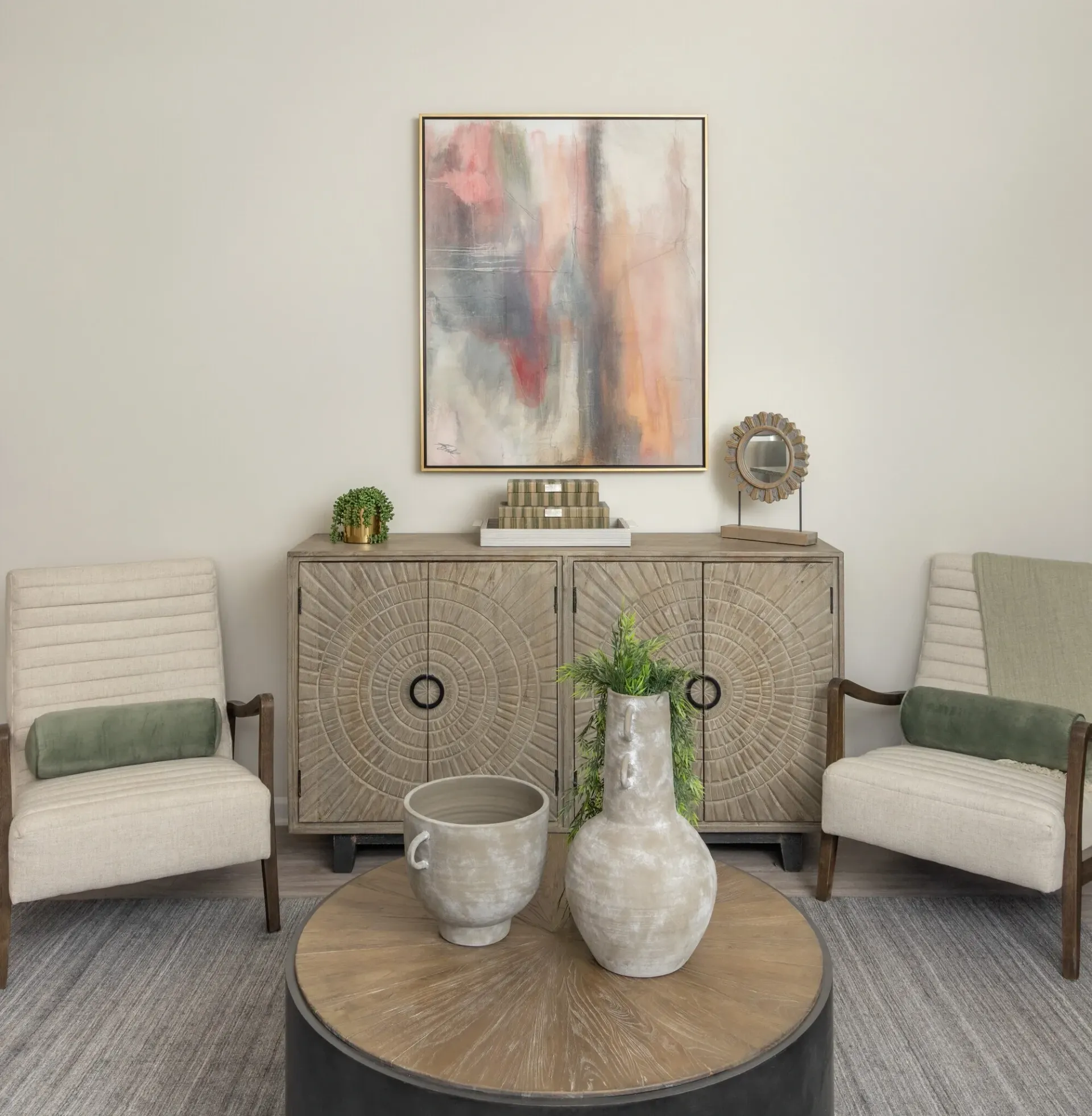 Living room with two chairs, a round coffee table, and a decorative cabinet with abstract art above.