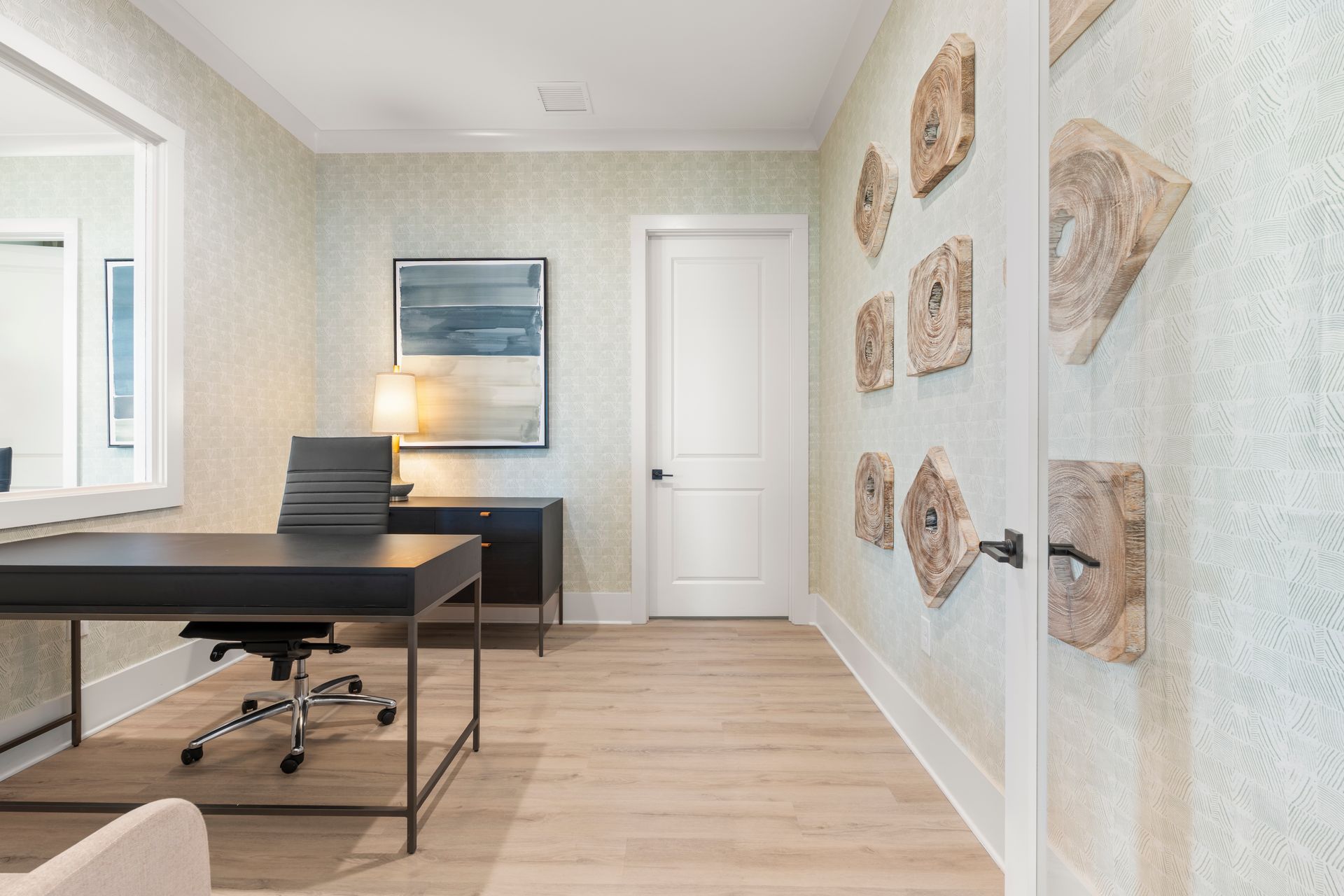 Bright home office with black desk, swivel chair, wall art, and white door on light wood floor