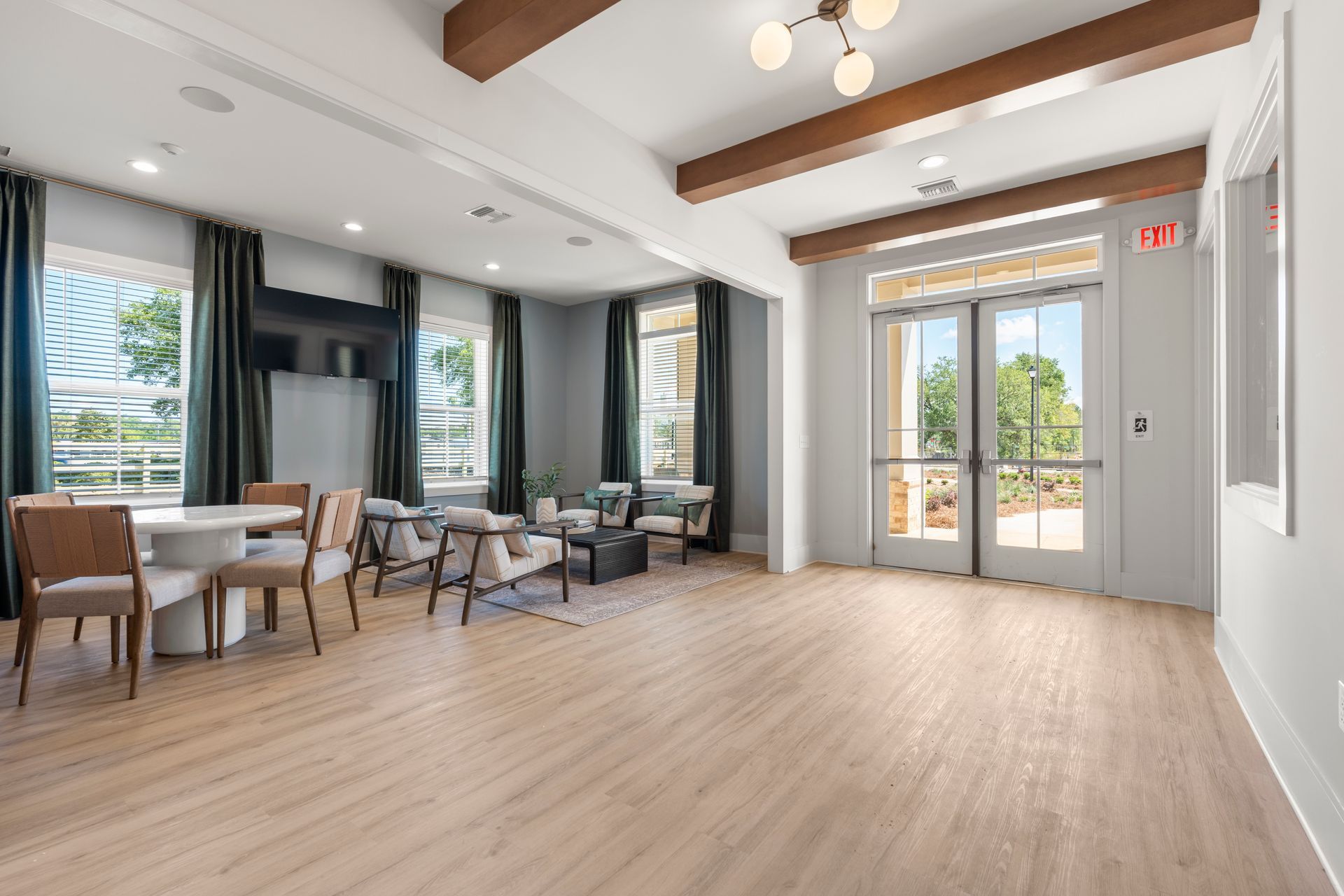Bright empty lobby with wood floors, ceiling beams, chairs, and glass doors/windows with outdoor views