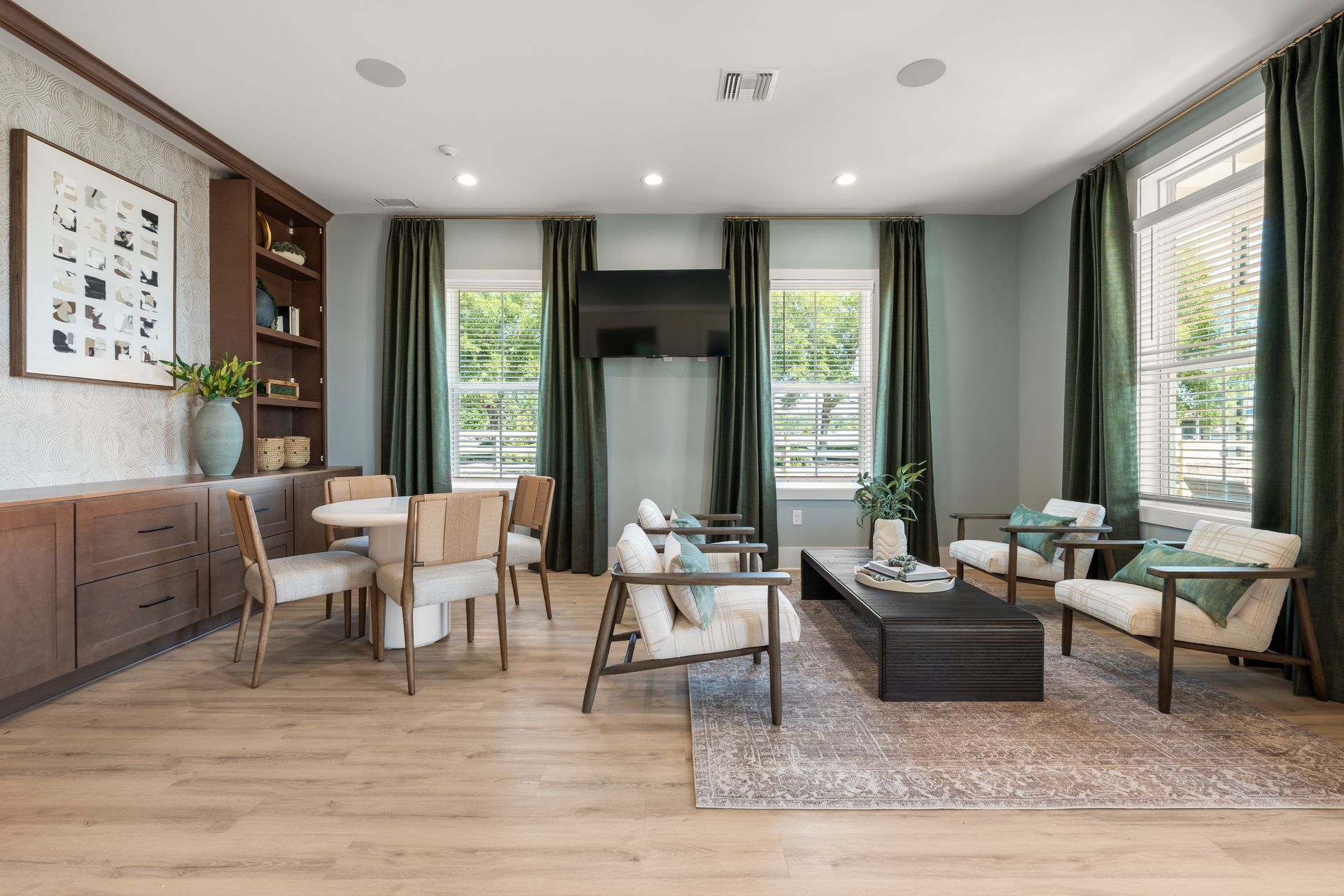 Modern living room with wooden floors, gray sofas, green curtains, and large windows.
