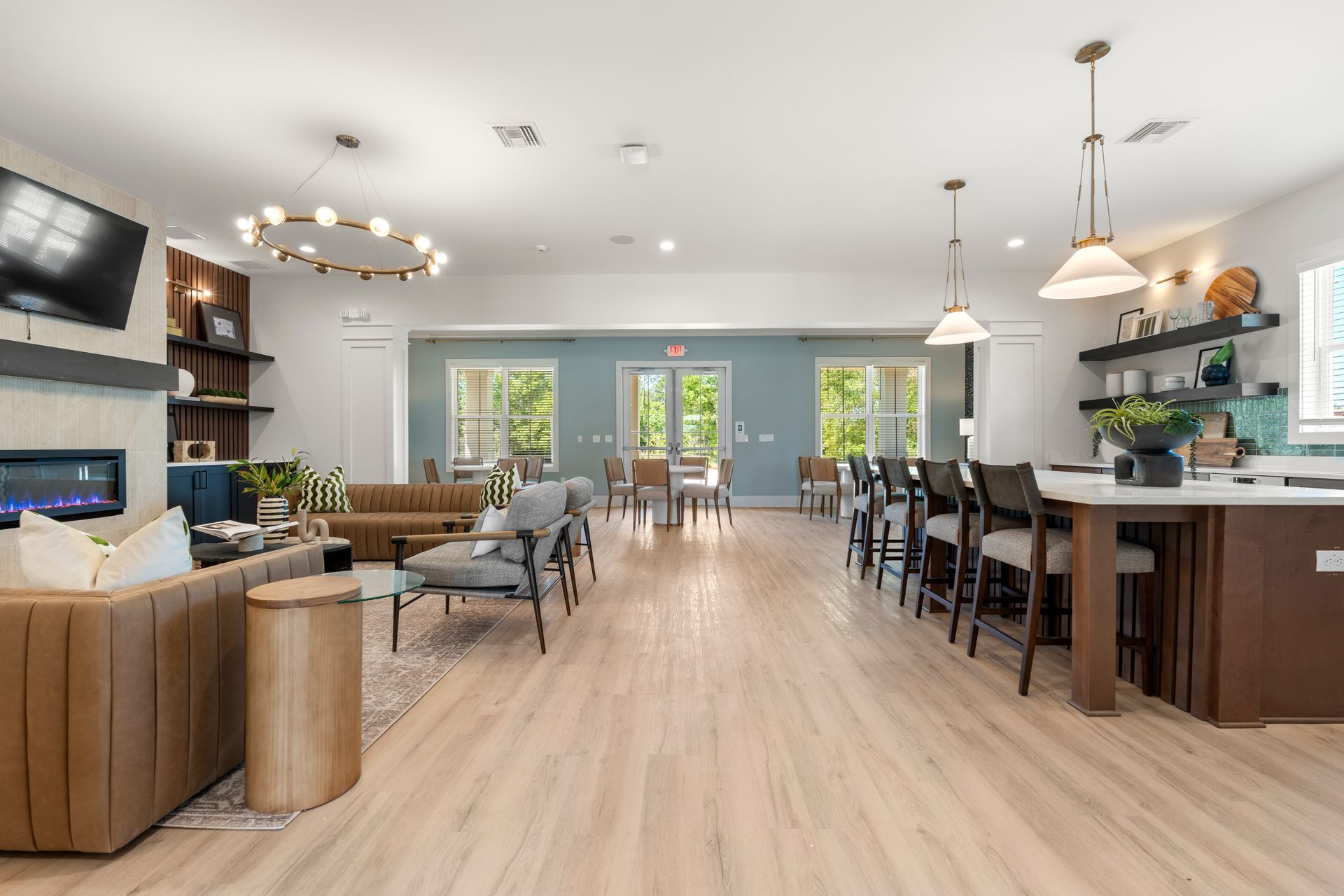 Open-concept kitchen and living room with light wood floors, island seating, and large windows leading outside