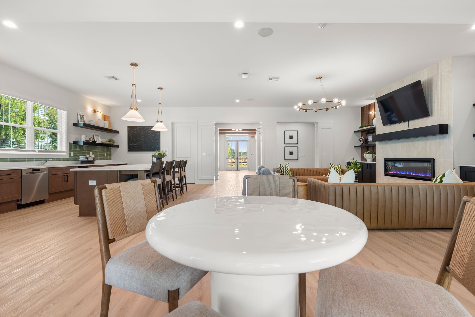 Modern open-concept living room and kitchen with beige seating, white table, and wall-mounted TV and fireplace.