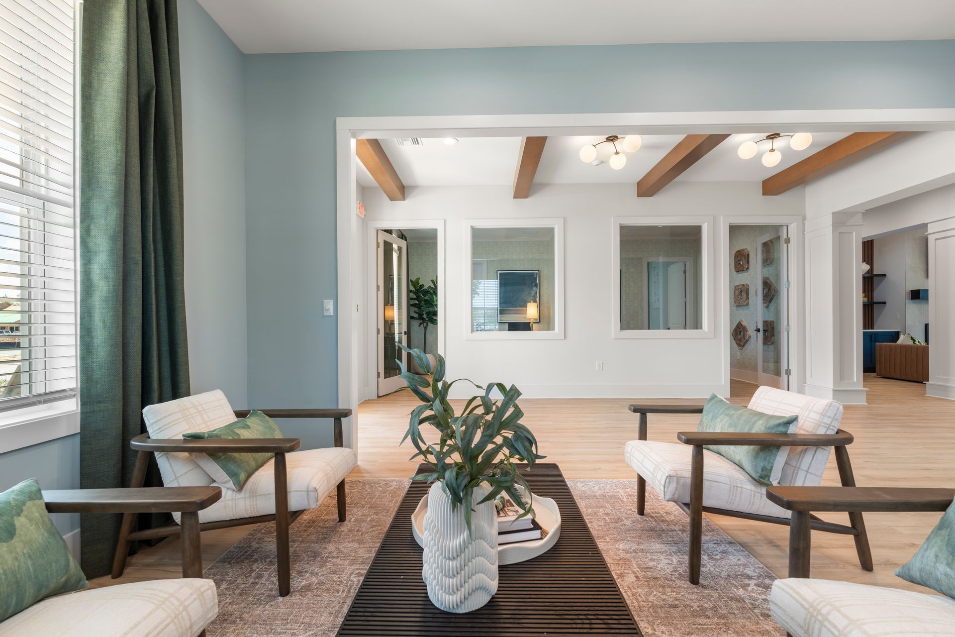 Bright living room with wooden beams, lounge chairs, rugs, and a central plant arrangement.