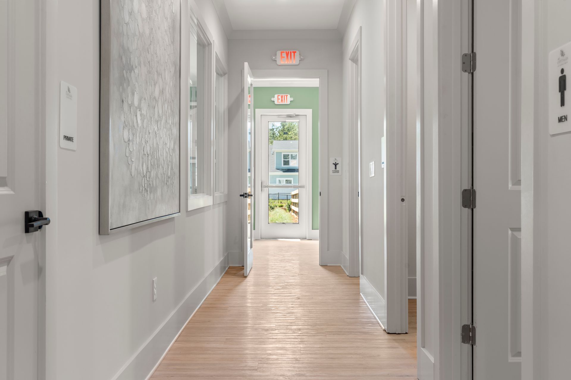 Bright hallway with white walls, light wood floor, and a glass door at the far end.
