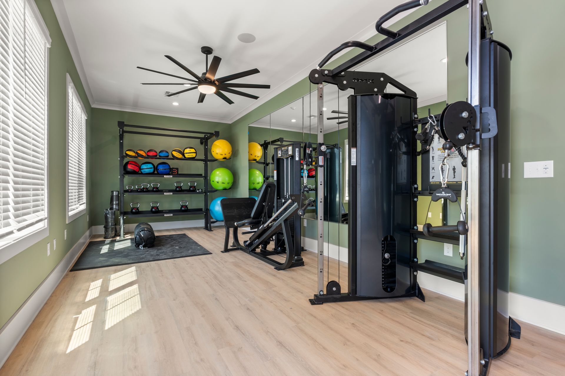 Modern home gym with weight machine, exercise bench, medicine balls, and large ceiling fan