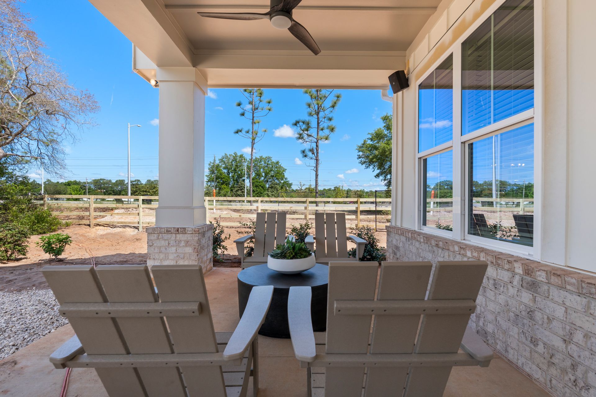 Covered patio with two beige chairs, a small table, and a view of the yard and sky
