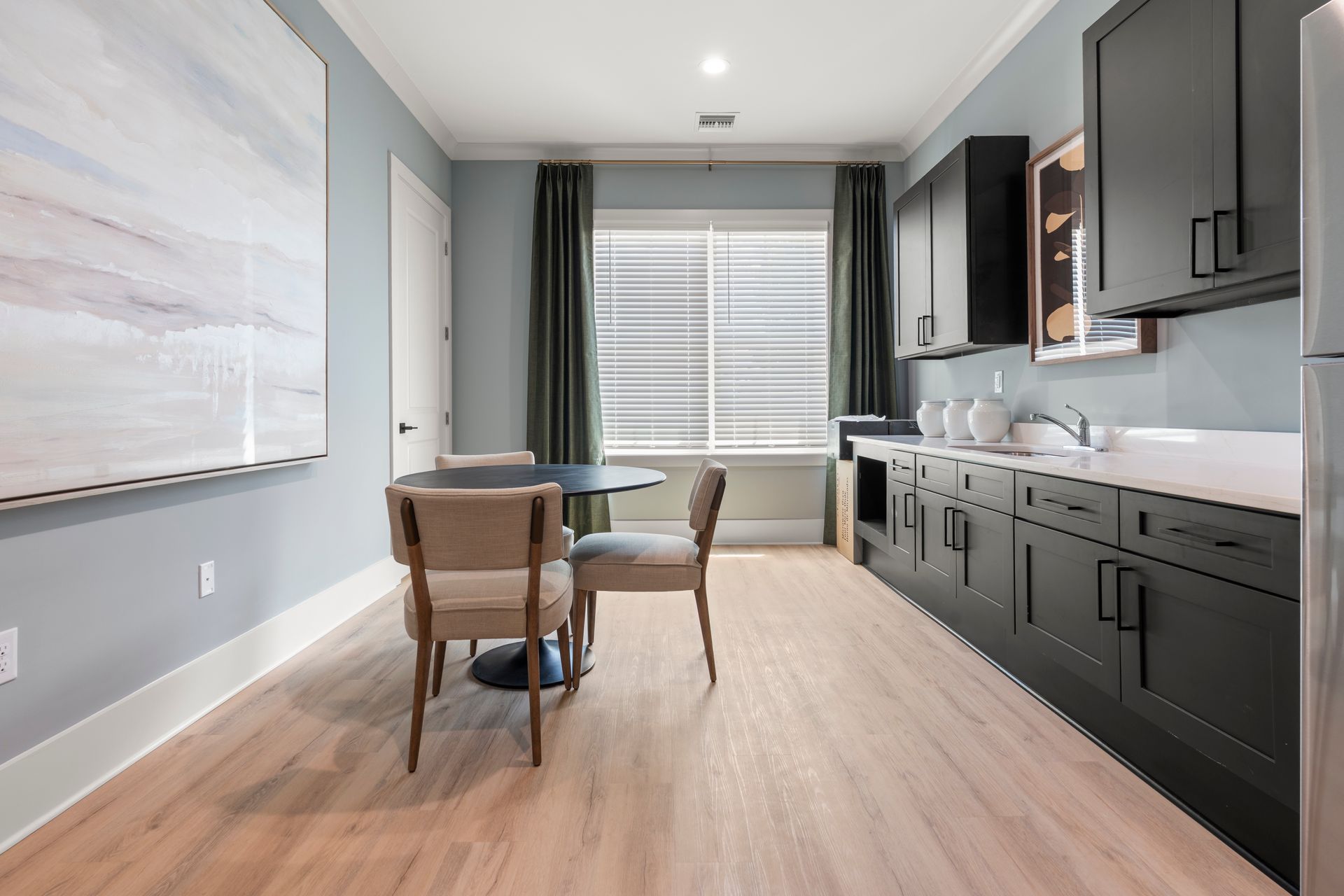 Modern kitchen with dark cabinets, wood floors, and a small dining table by a bright window