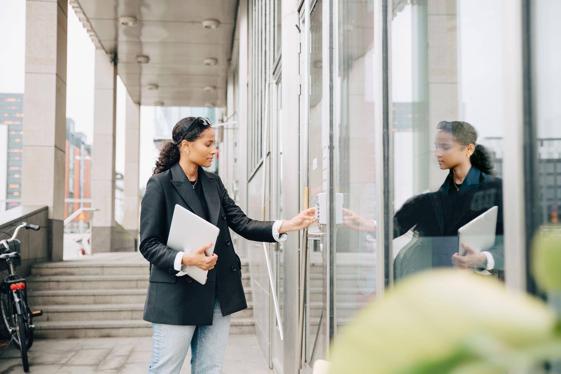 A woman is standing in front of a building holding a laptop.