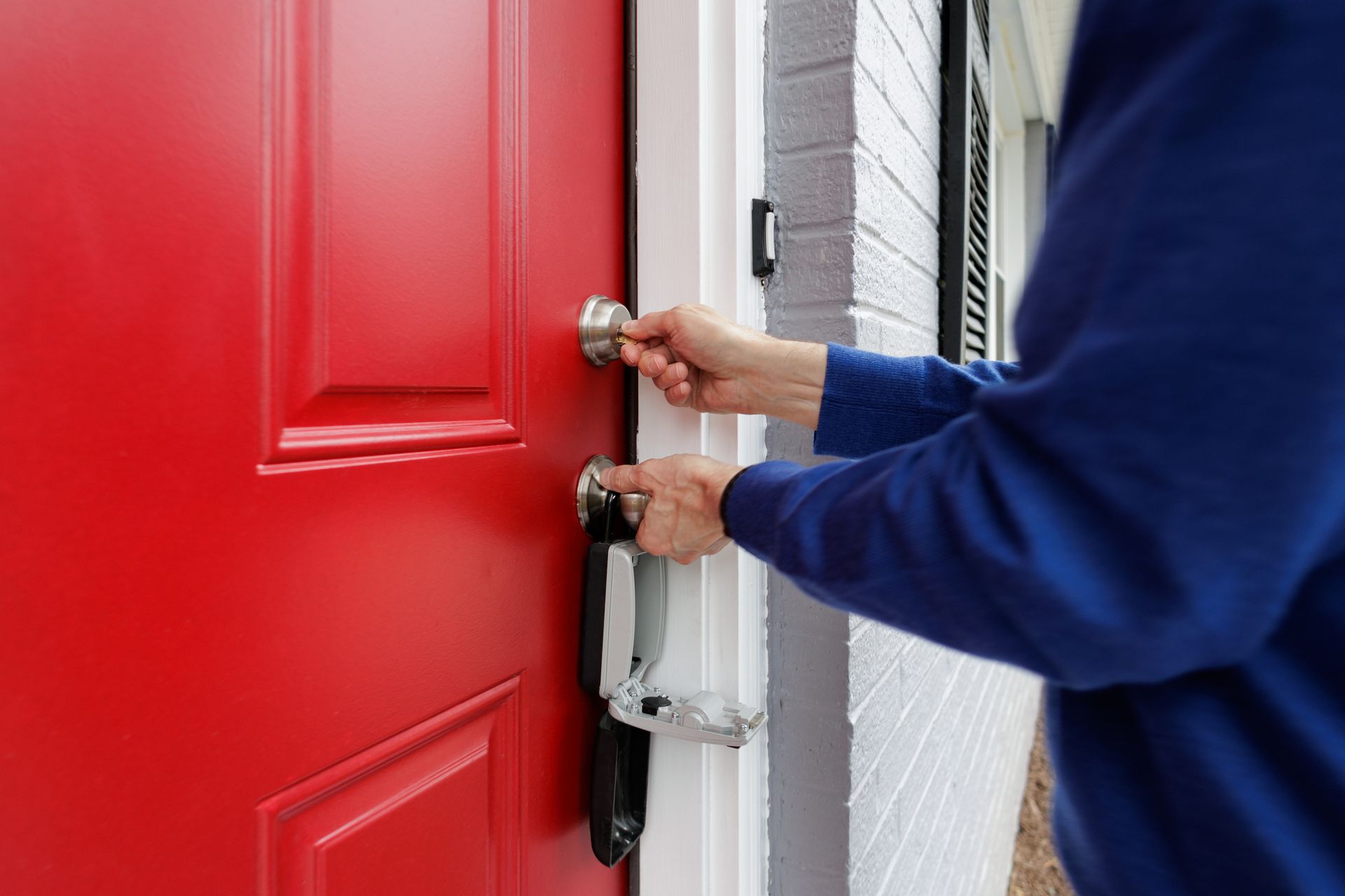 A person is opening a red door with a key.