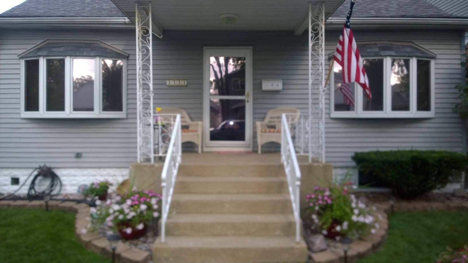 A house with stairs leading up to the front door and an american flag on the porch.