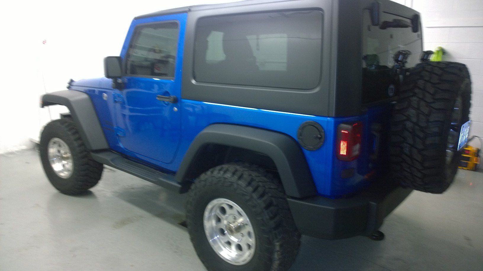 A blue jeep with a black top is parked in a garage.