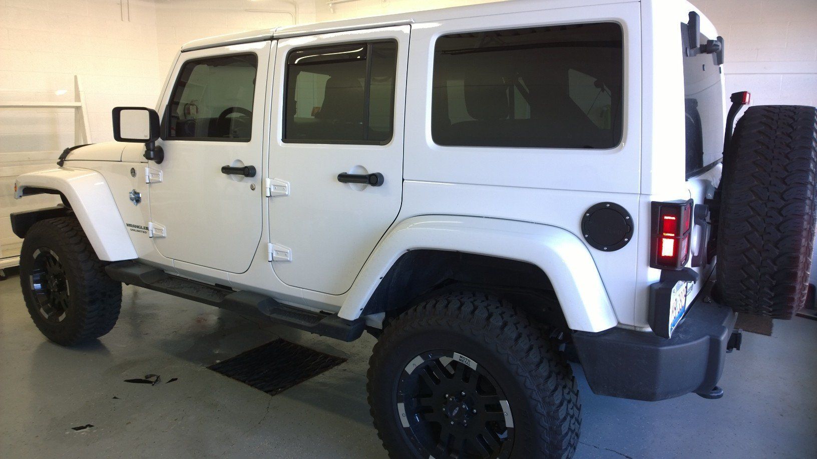 A white jeep is parked in a garage with black tires