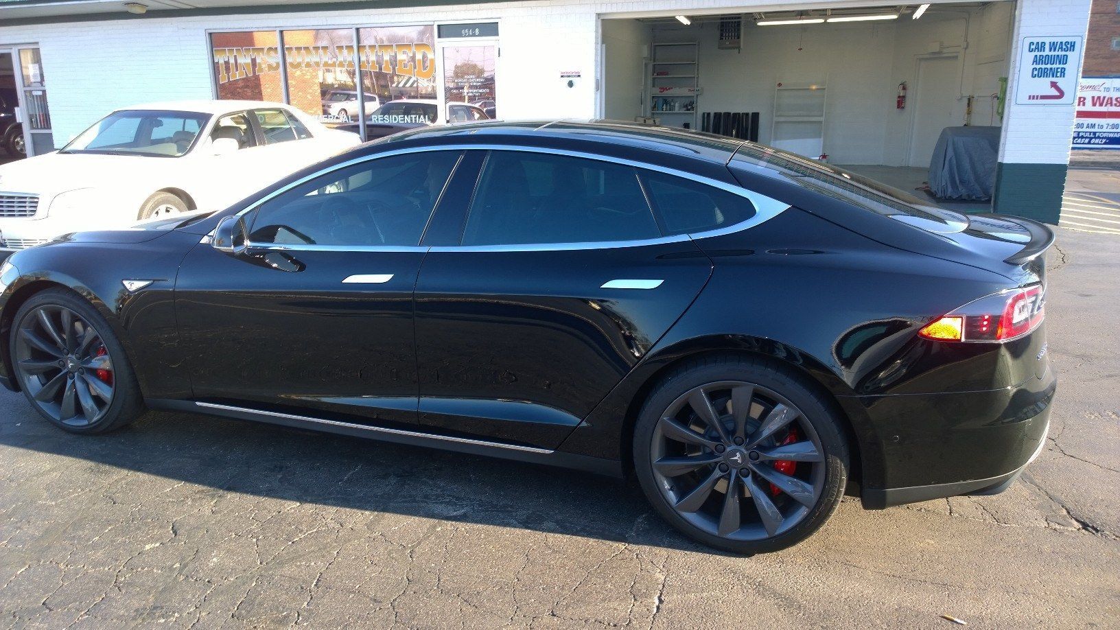 A black tesla model s is parked in front of a garage.