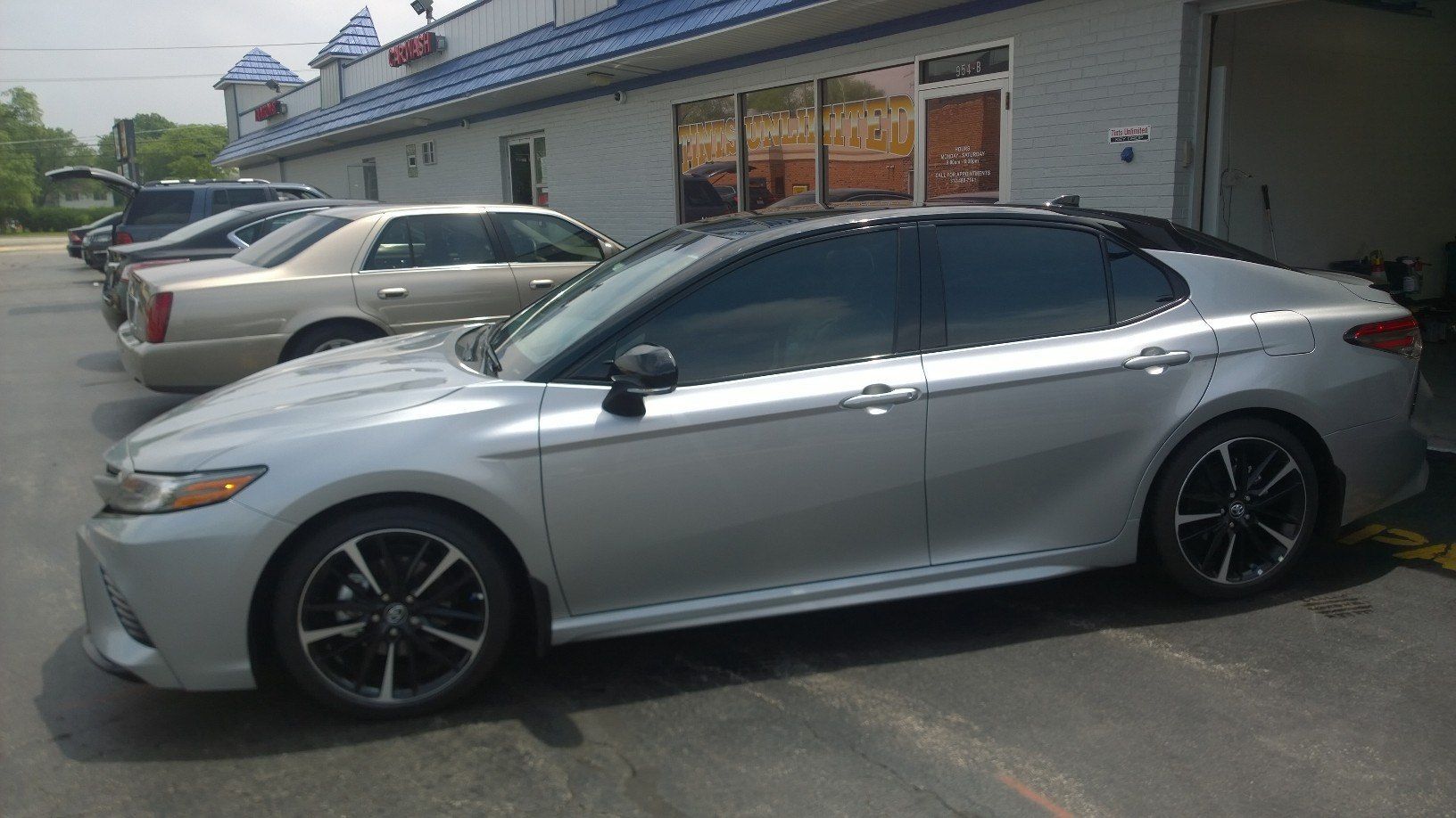 A silver car is parked in a parking lot in front of a building.