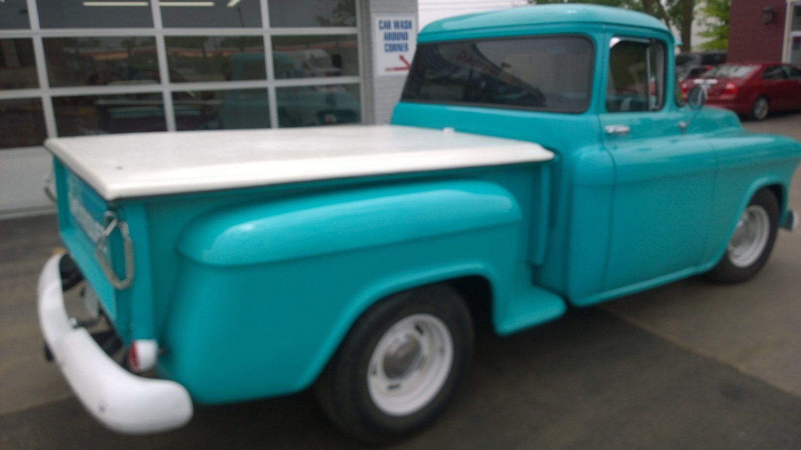 A blue truck with a white top is parked in front of a garage.