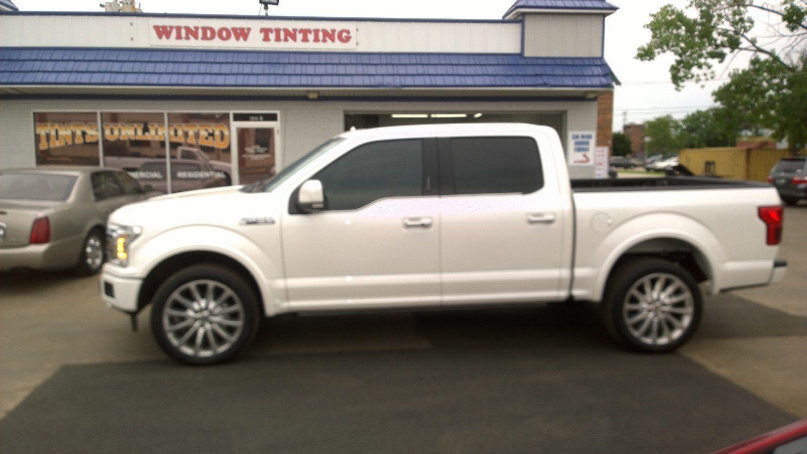 A white pickup truck is parked in front of a window tinting shop.