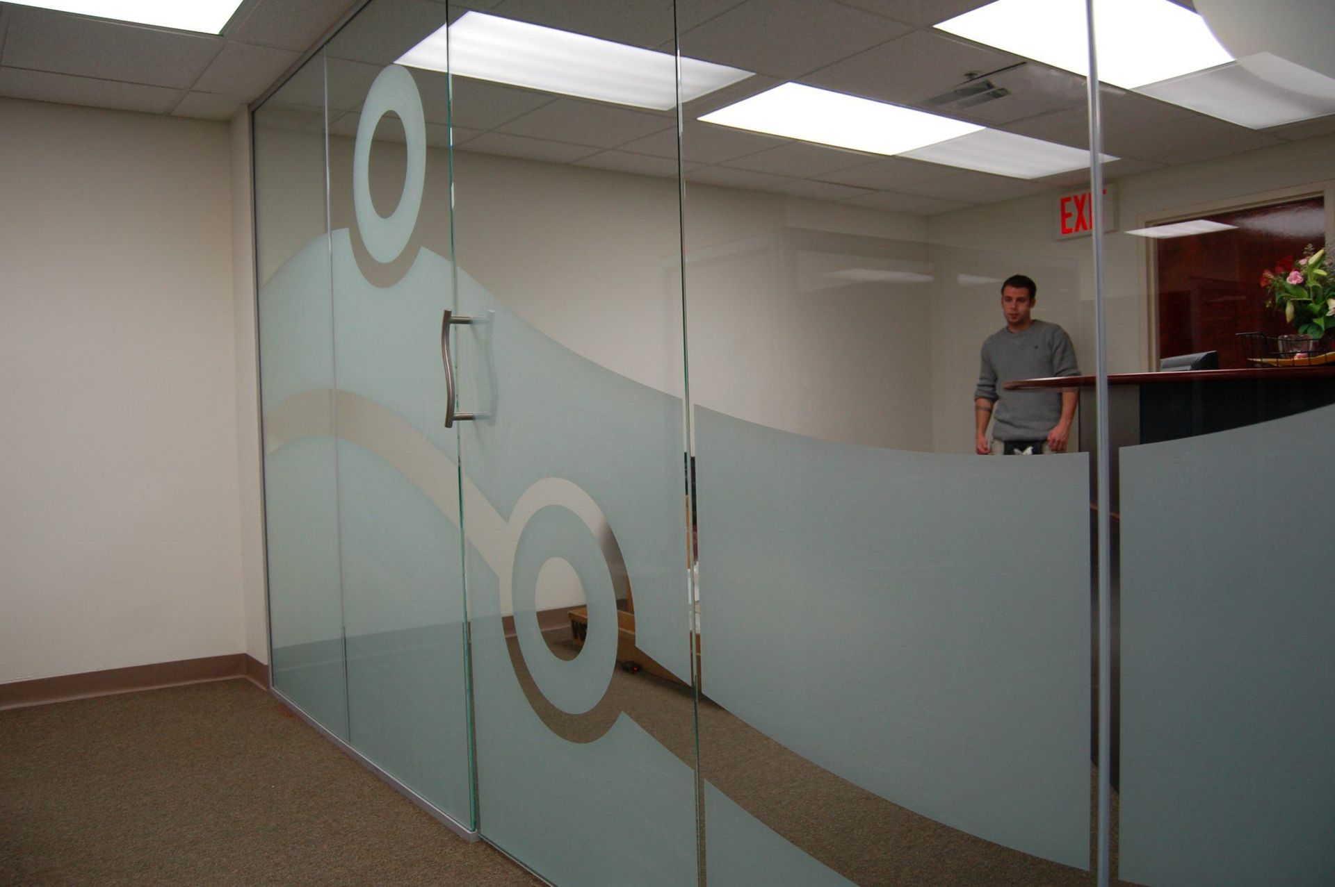 A man stands behind a glass wall with a target on it