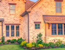 A large brick house with a lot of windows and a lush green lawn in front of it.