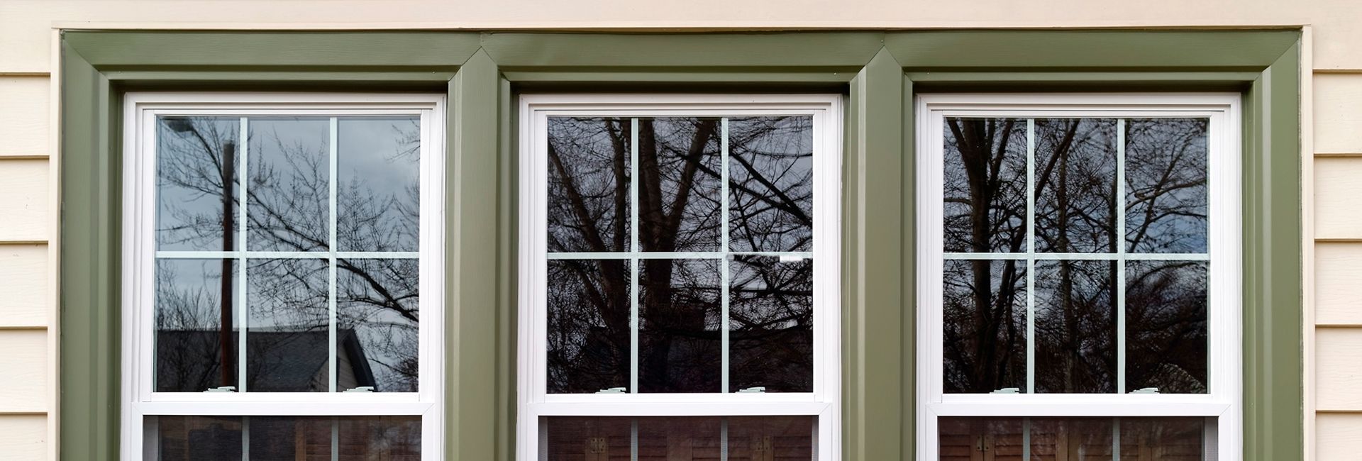 A close up of three windows on a house with trees reflected in the windows.