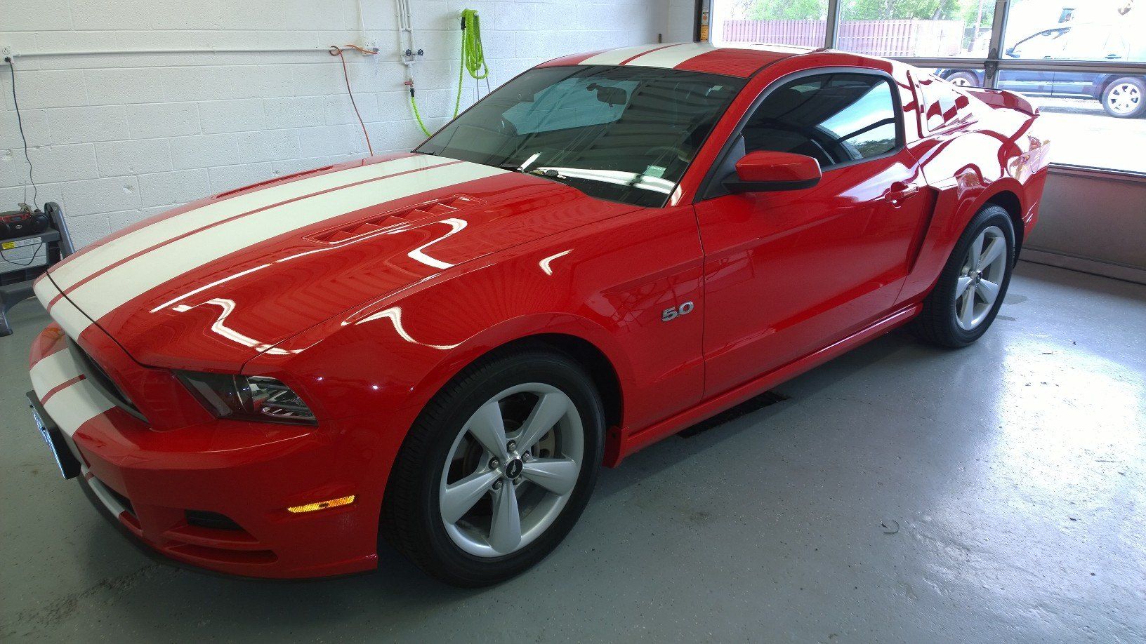 A red mustang with white stripes on the hood is parked in a garage.
