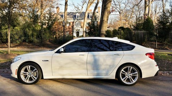 A white car is parked on the side of the road in front of a house.