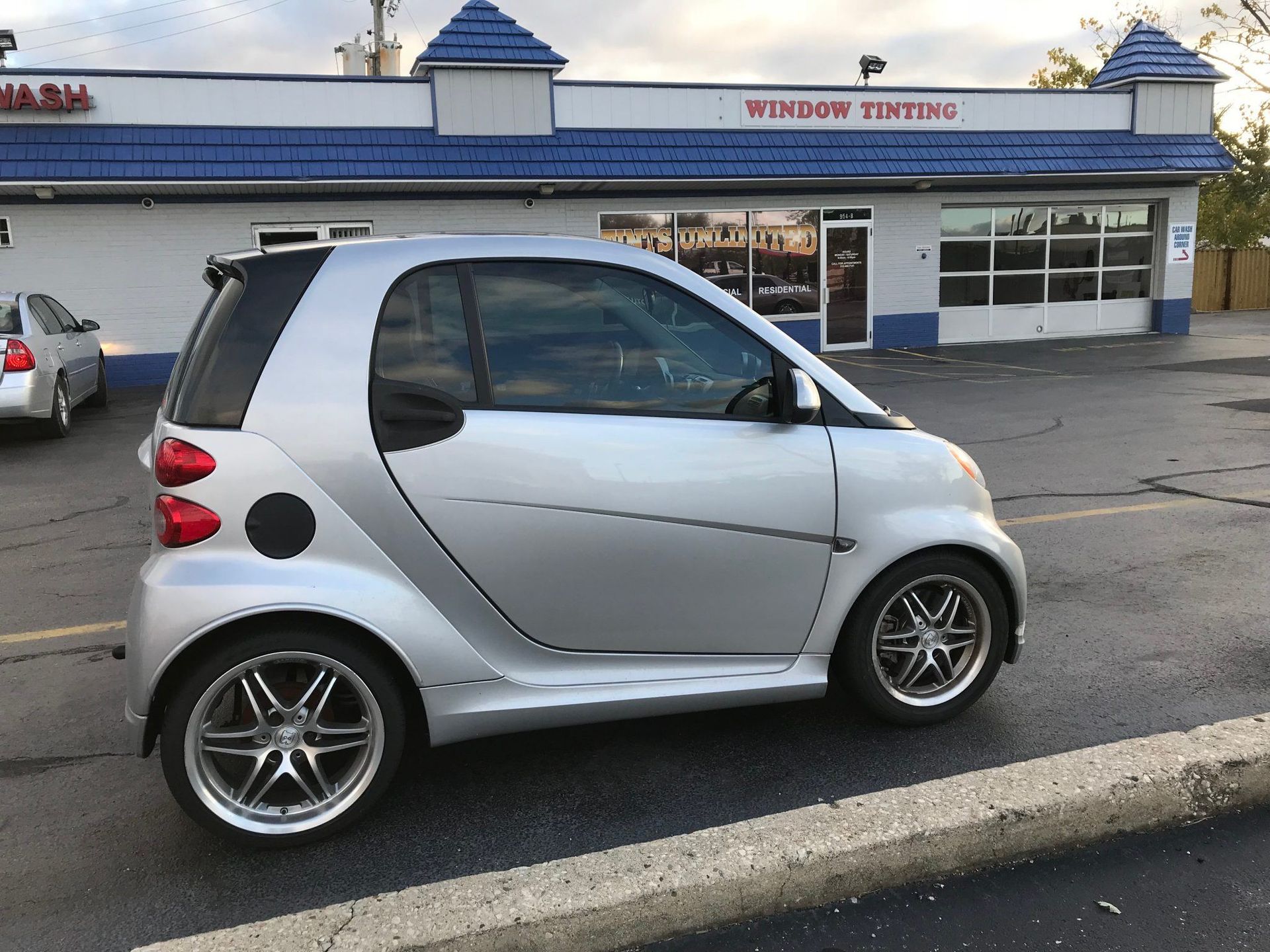 A silver car is parked in front of a window tinting shop