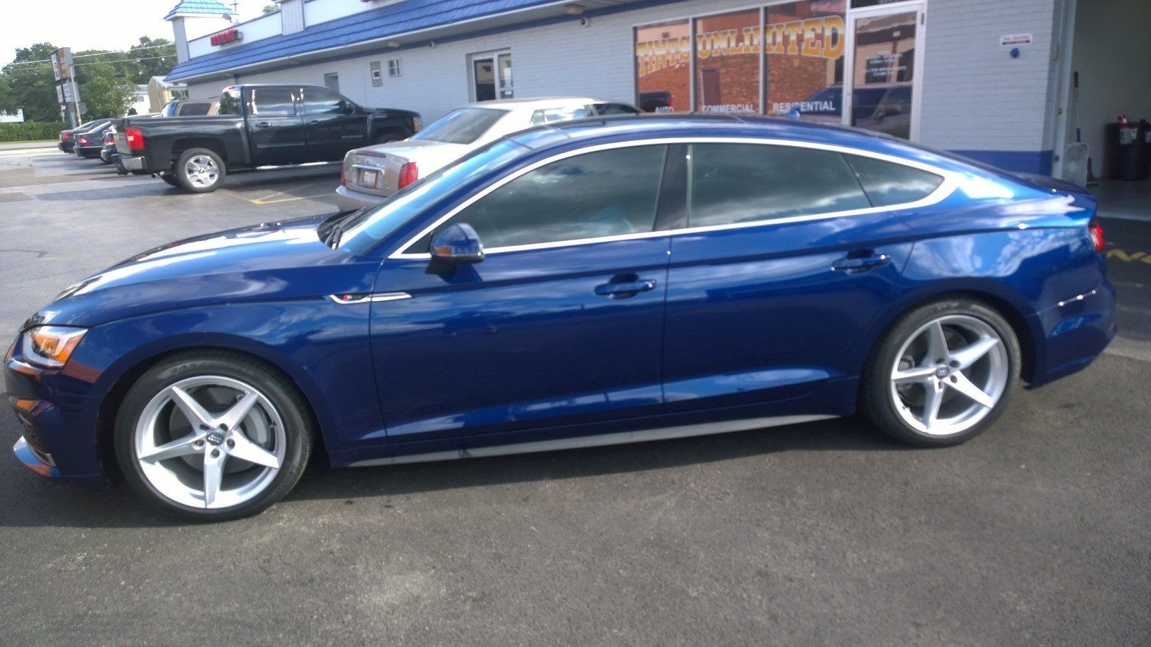 A blue car is parked in a parking lot in front of a building.