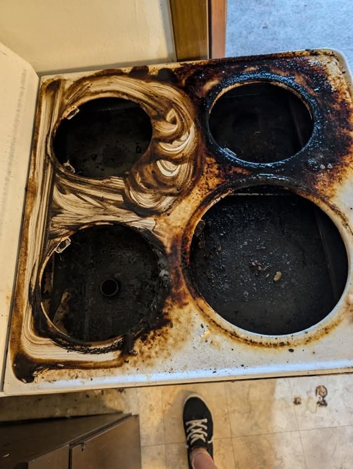 A person is standing on a very dirty stove top.