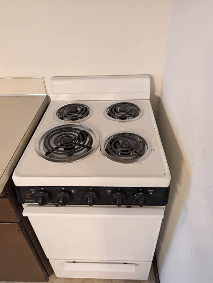 A white stove with four burners is sitting in a kitchen.