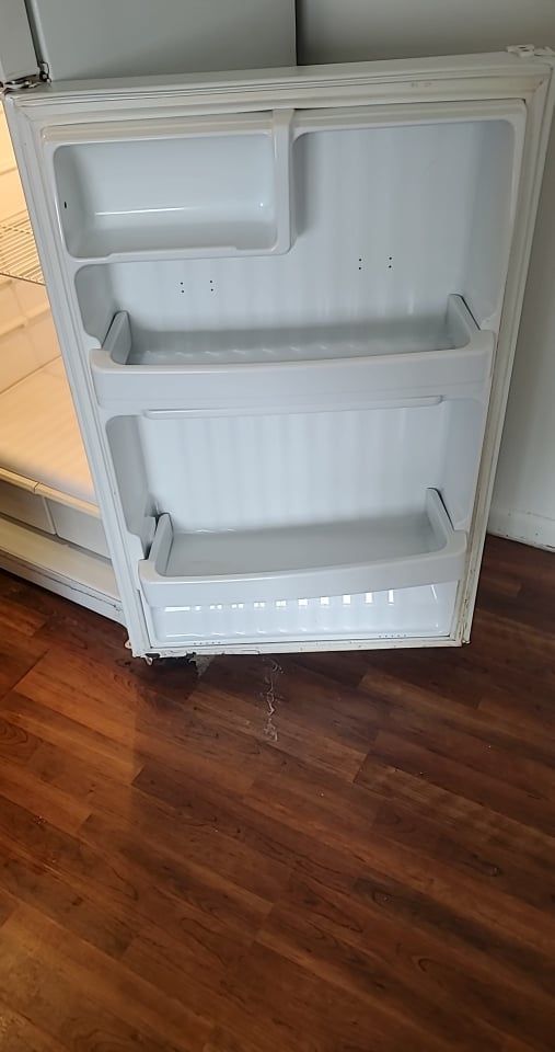 An empty refrigerator is sitting on a wooden floor.