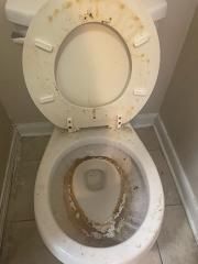 A dirty toilet in a bathroom with the lid open.